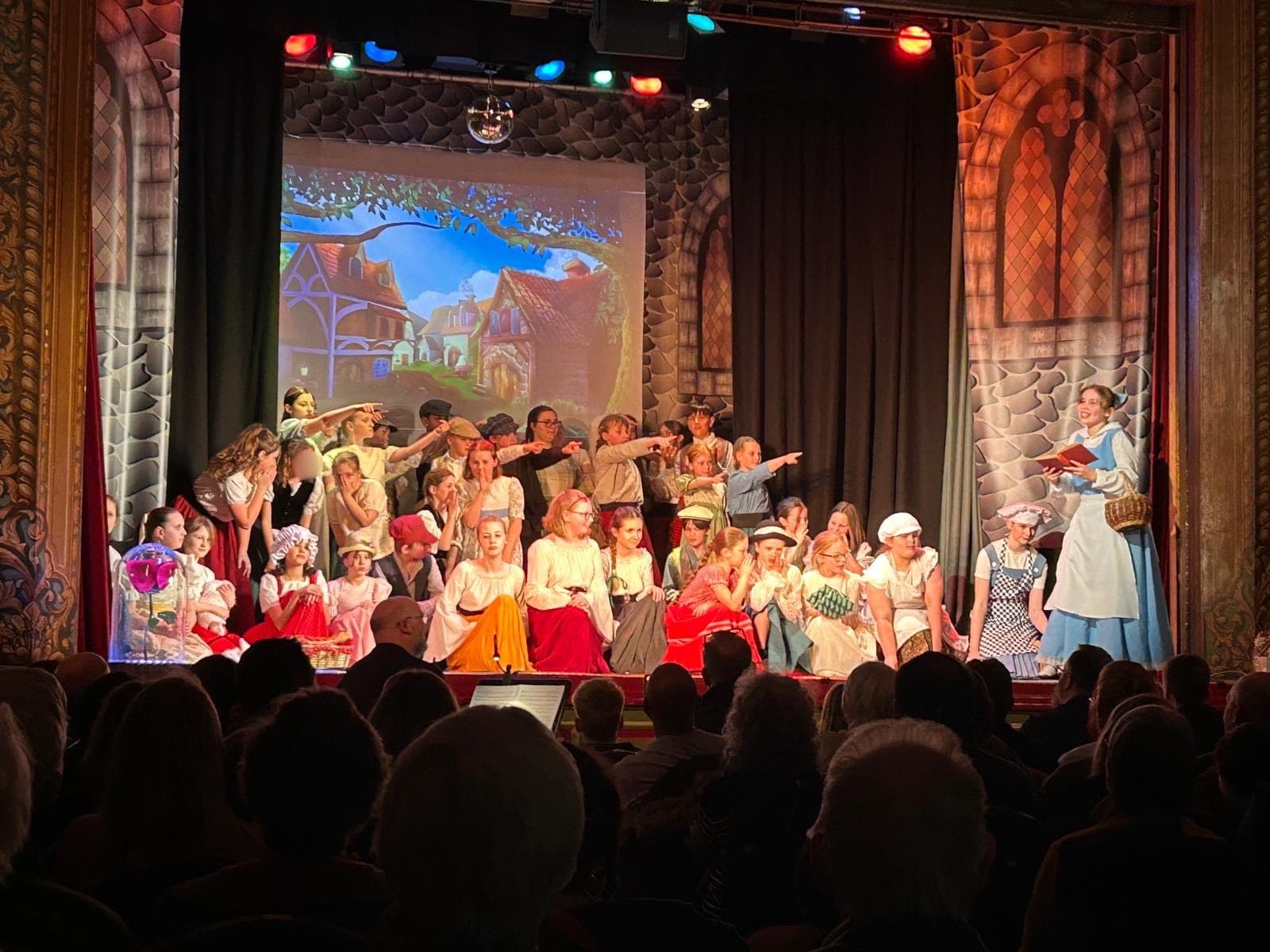 The village ensemble in the opening scene of Beauty and the Beast, Belle reading at front of stage