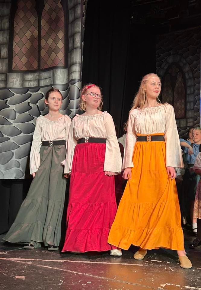 Three village girls in green, red, and yellow peasant dresses